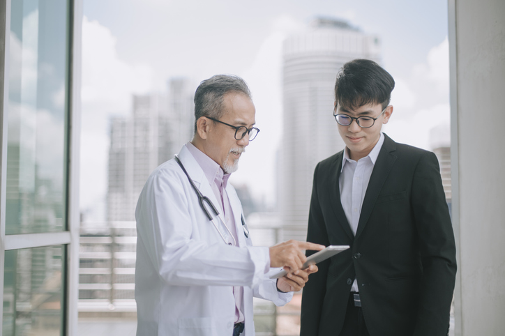 asian chinese doctor talking to his colleague at walkway showing medical report using digital tablet